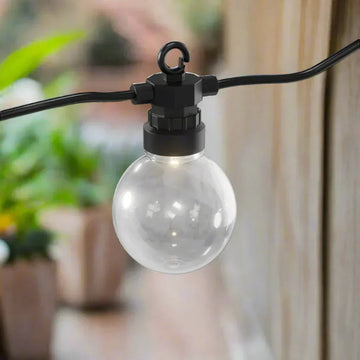 Transparante ronde LED buitenlamp aan zwarte kabel op terras, sfeervolle tuinverlichting