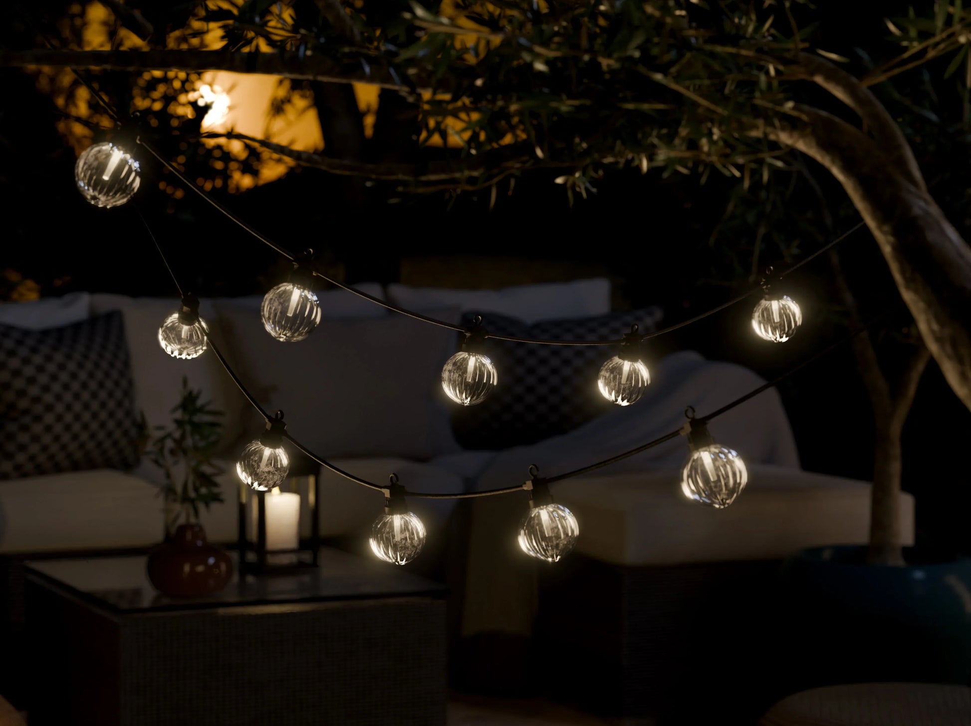 Sfeervolle buitenverlichting met bolvormige LED-lichtslinger, loungehoek en kaars op tafel