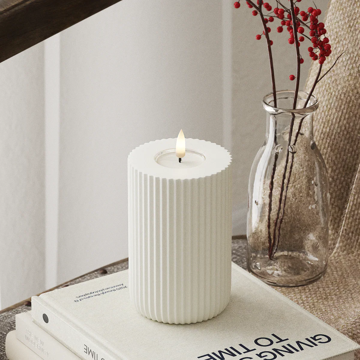 Moderne witte LED-stompkaars met 3D-vlam van Nordic Flame op tafel, naast glazen vaas.