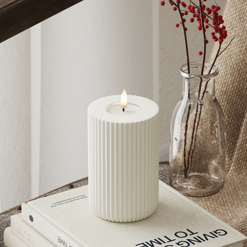 Moderne witte LED-stompkaars met 3D-vlam van Nordic Flame op tafel, naast glazen vaas.