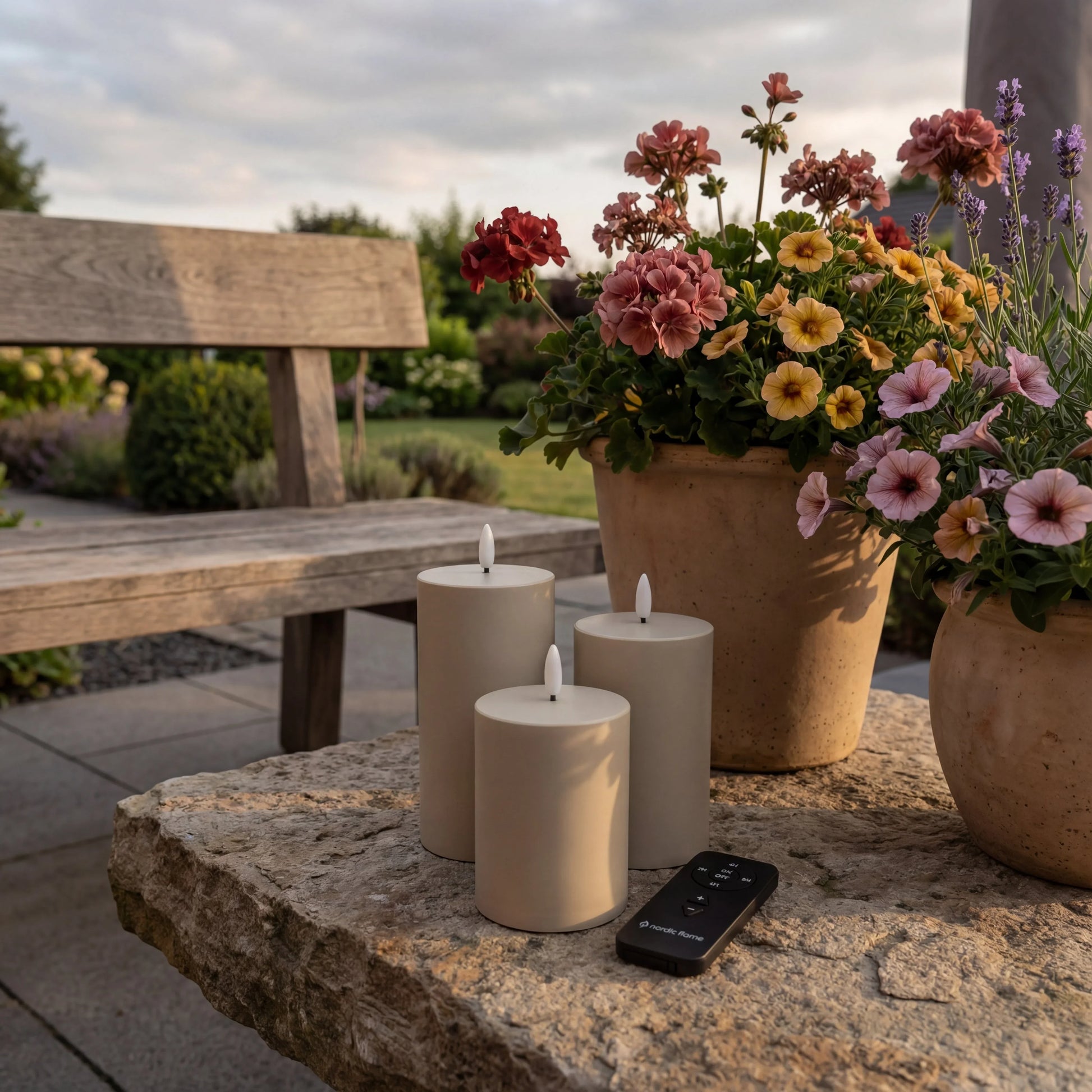Outdoor Nordic Flame LED-kaarsen set met afstandsbediening op tuintafel, bloemen op achtergrond.