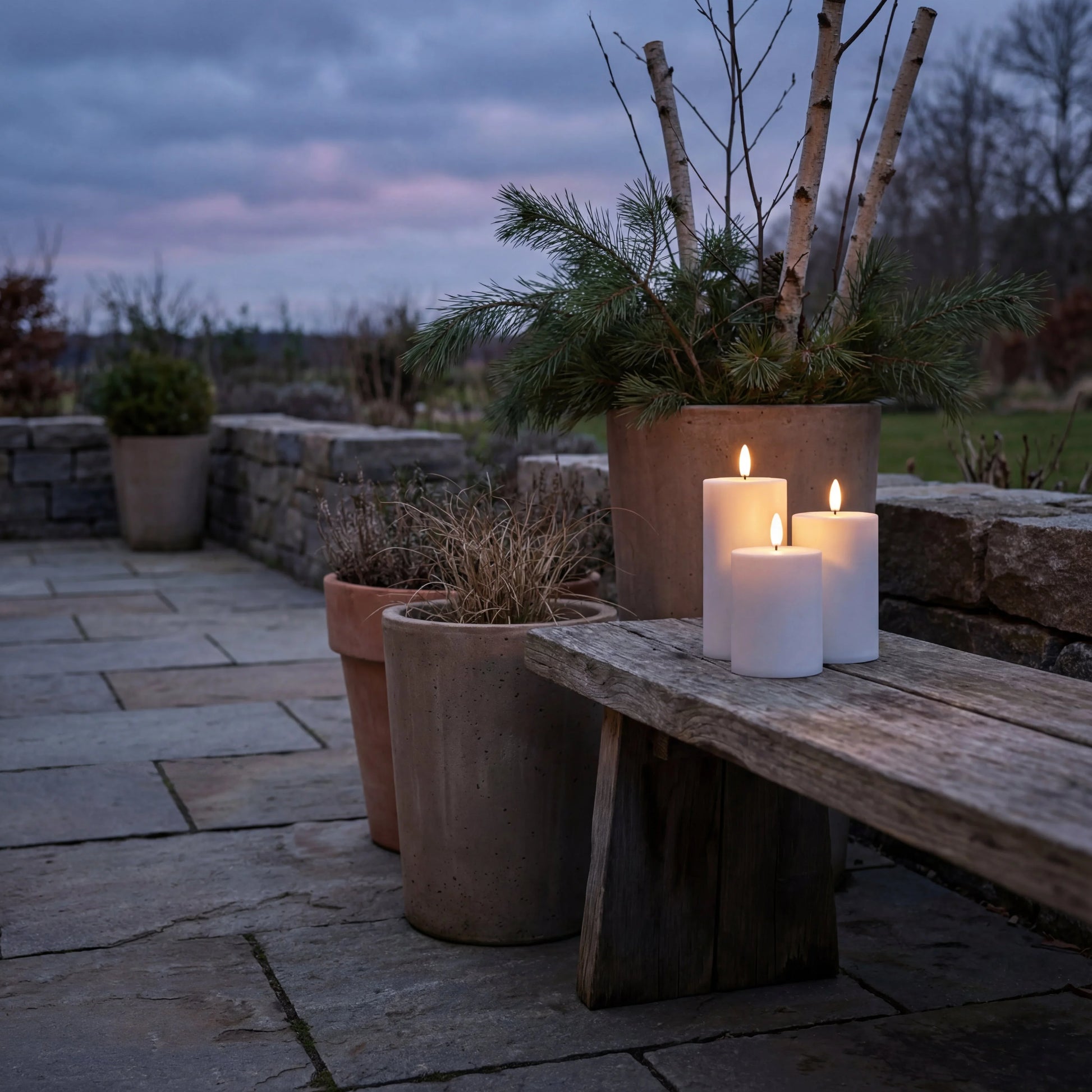 Drie witte Nordic Flame LED-kaarsen met 3D-vlam op buitenbank, sfeervol terras.